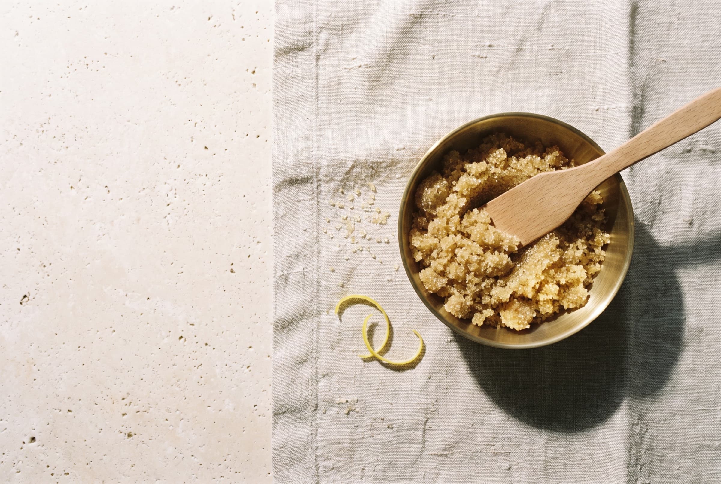 Golden sugar scrub in a brass bowl with a wooden spatula